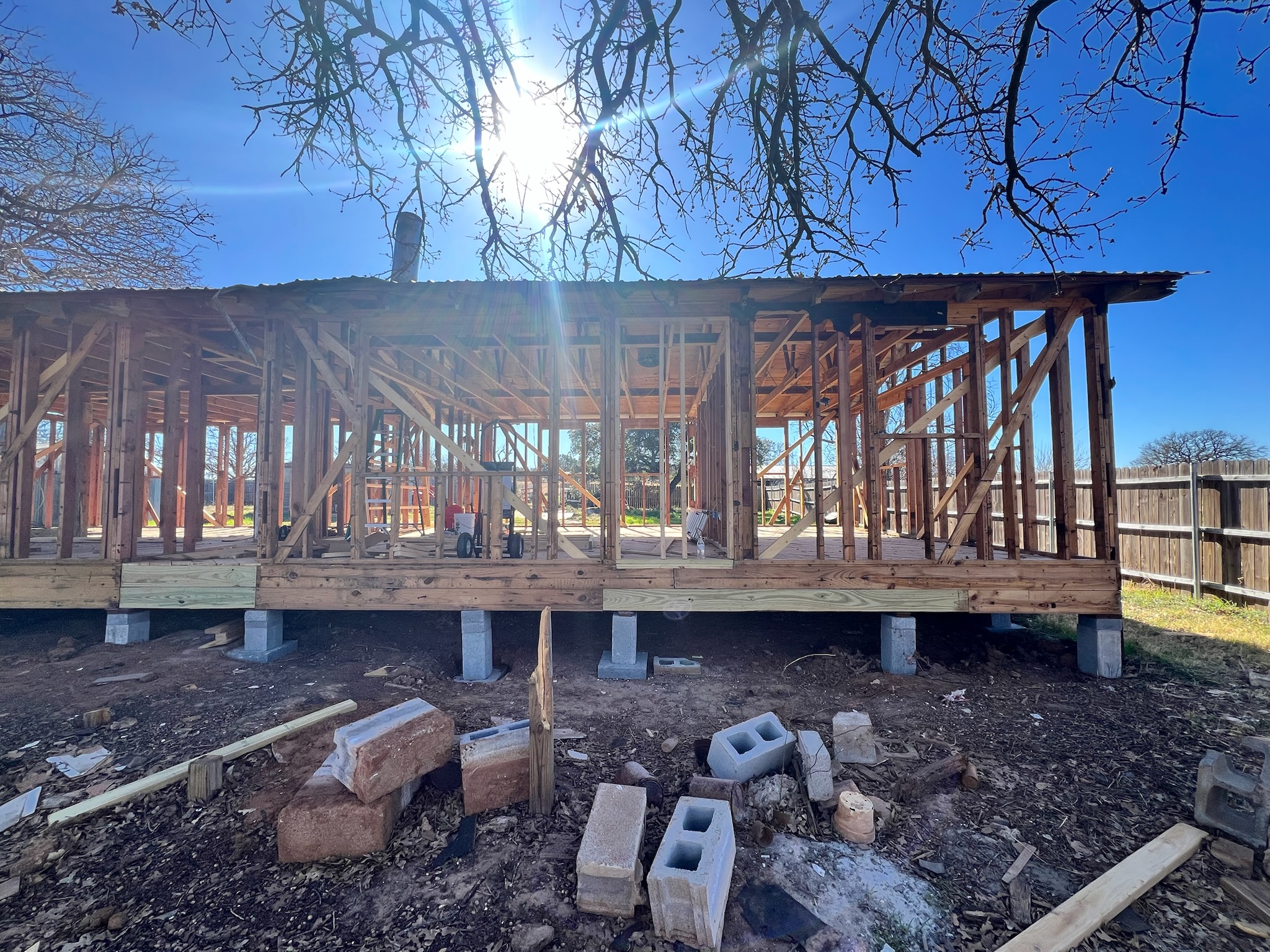 The framed skeleton of one of the outbuildings, photographed head-on with sun flare.